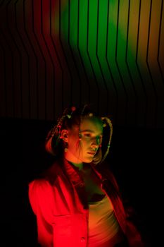 A stylish woman with braided hair poses under vibrant red and green lighting for a fashion photoshoot.