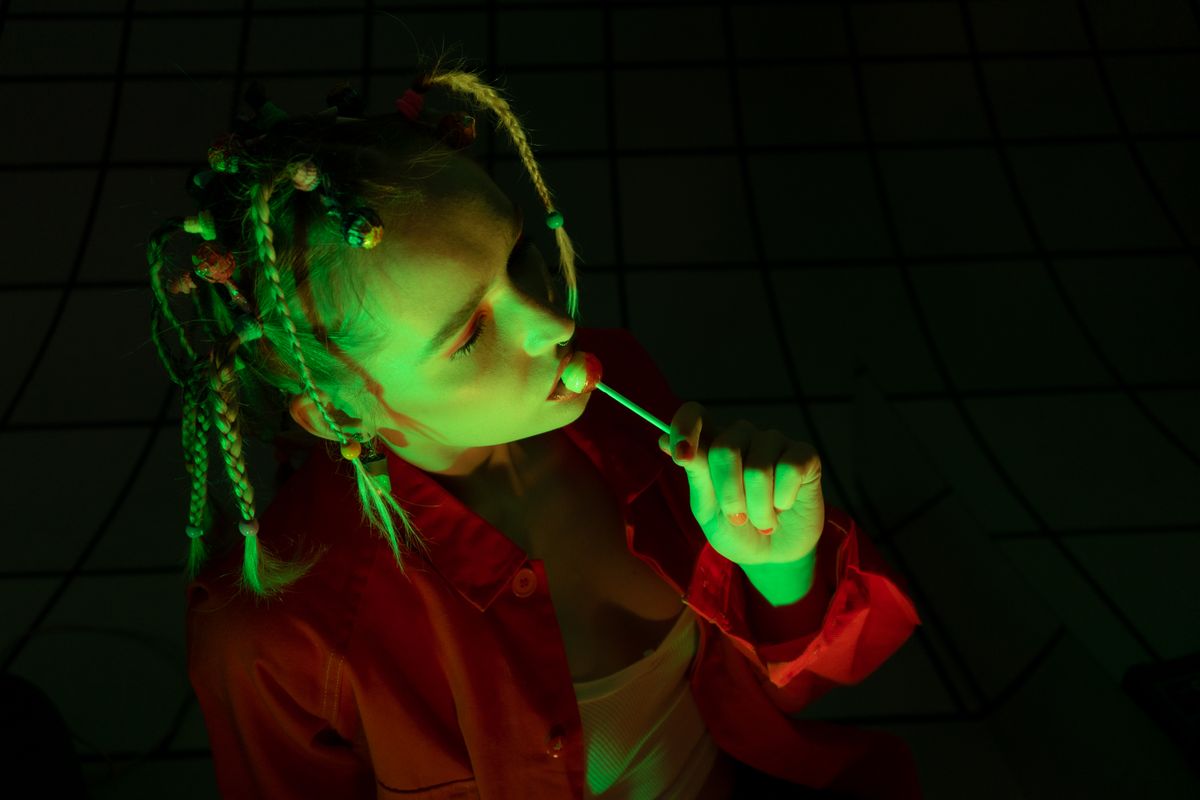 Artistic portrait of a woman with neon lighting holding a lollipop, showcasing unique fashion style.