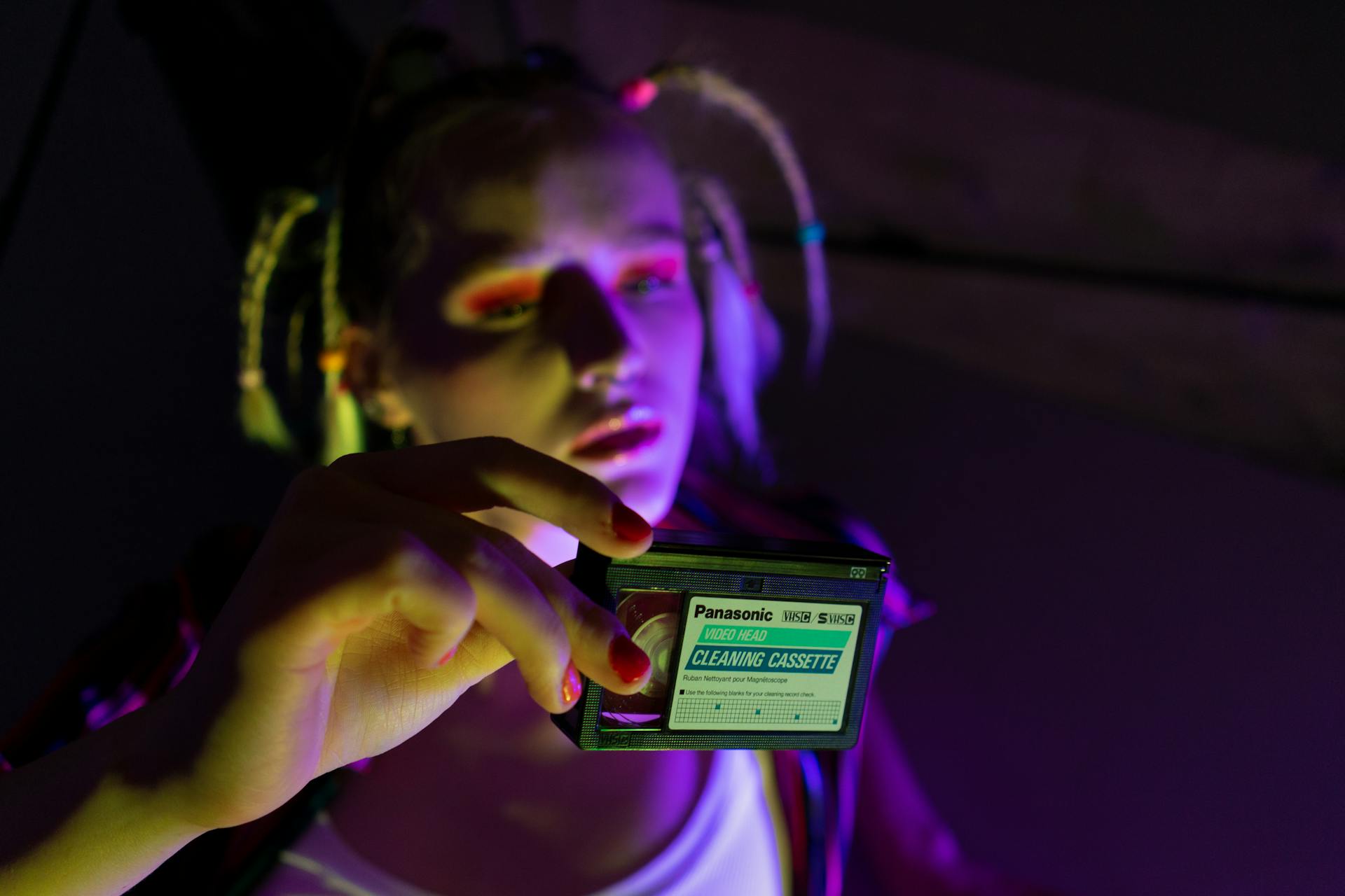 Portrait of a fashionable person holding a Panasonic cleaning cassette, with bold makeup and lighting effects.