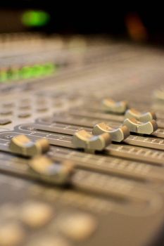 Close-up of a professional sound mixer in a studio with focus on slide controls and knobs.