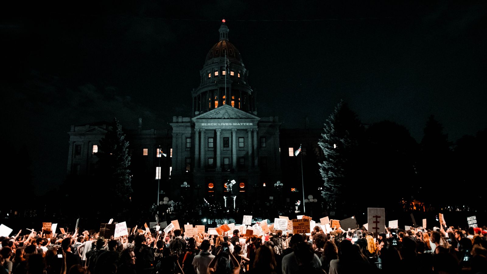 A large crowd protesting for civil rights at night in front of the Denver Capitol building.