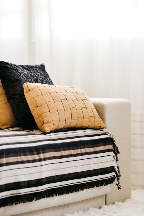 Stylish pillows and plaid on comfortable couch placed in light cozy living room