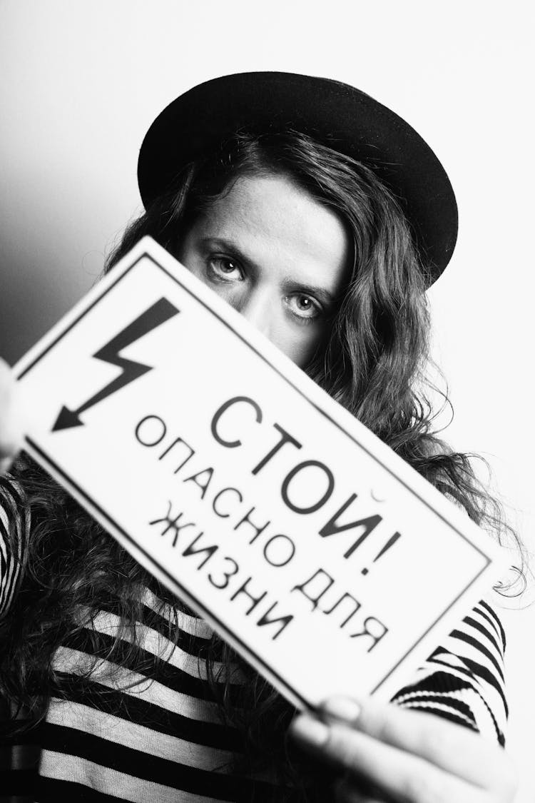 A Woman In Black Hat Holding A Sign Board While Seriously Looking At Camera