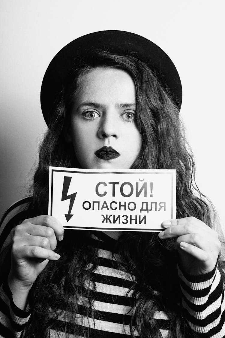 Grayscale Photography Of A Woman Holding A Small Sign 