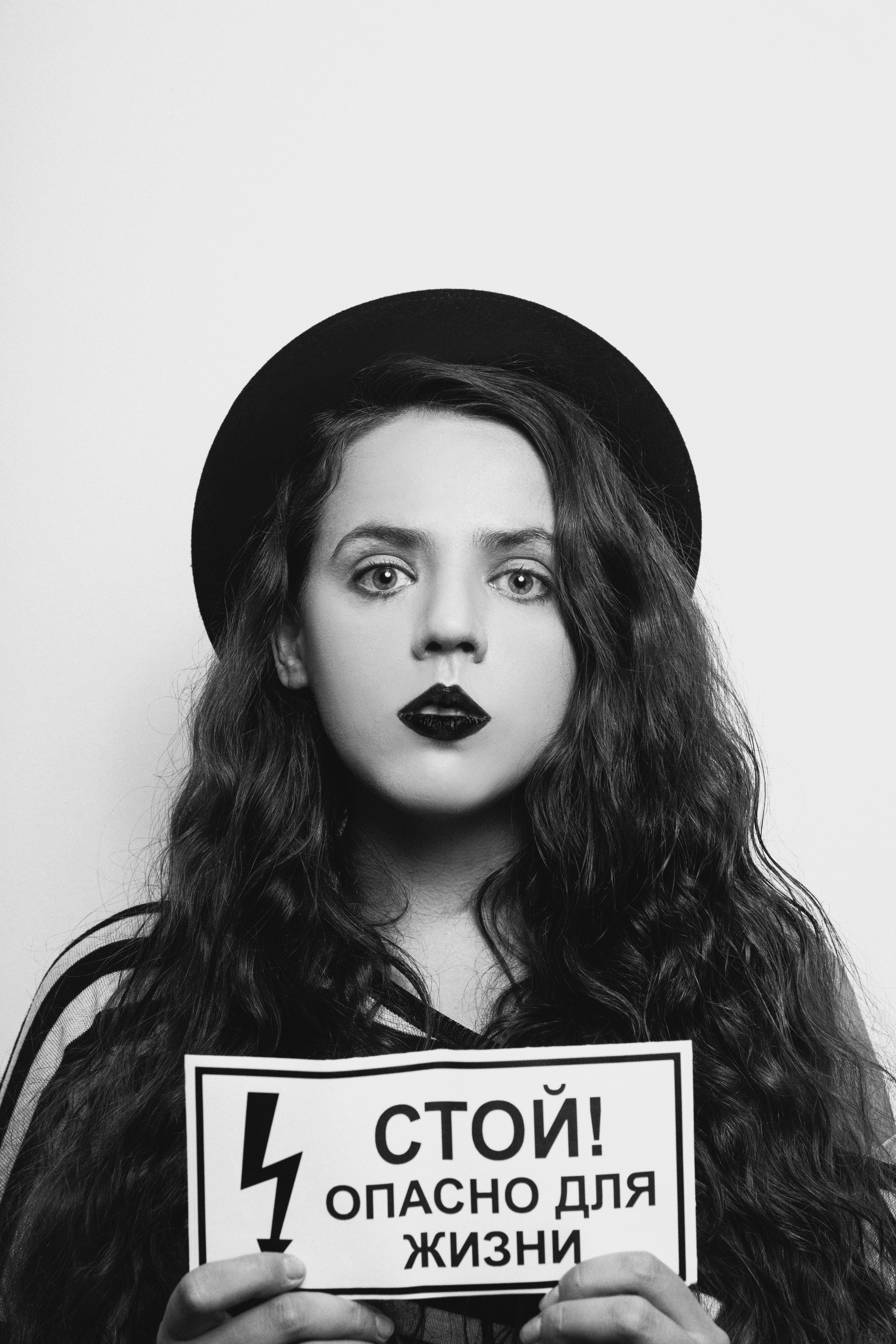 Black and white portrait of a woman holding a warning sign with serious expression.