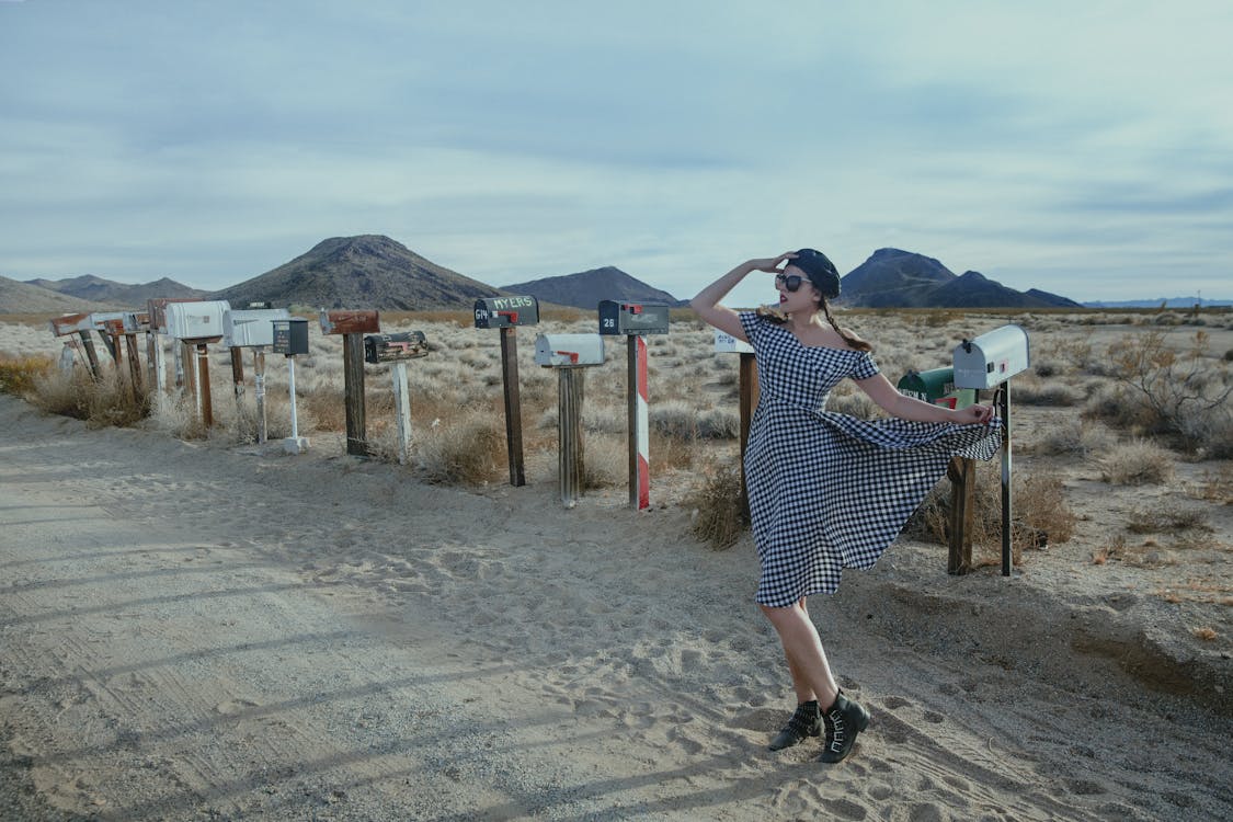 Woman in Black and White Dress Standing on Sandy Ground while Looking ...