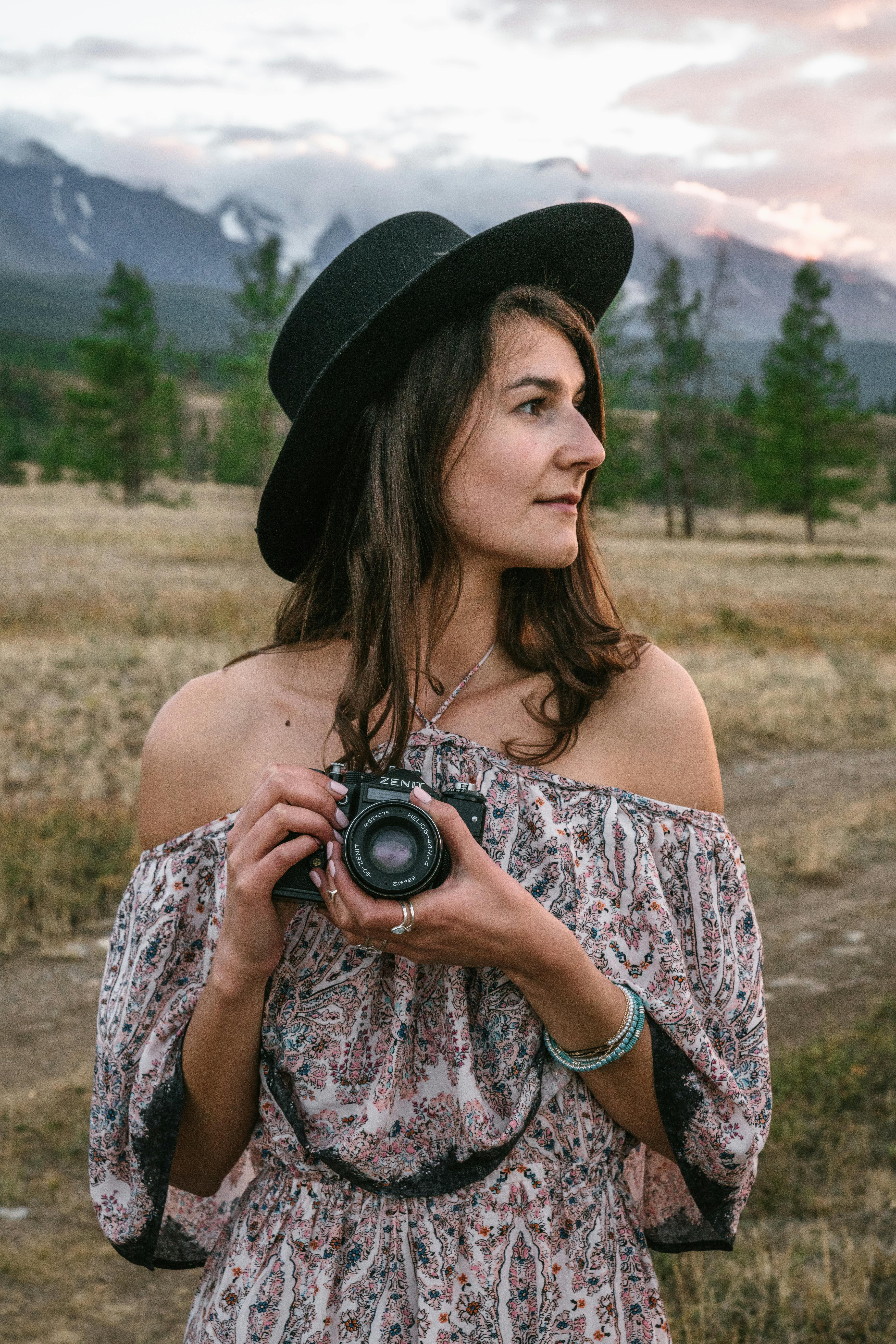 Young woman holding a camera in a picturesque mountain landscape at sunset.