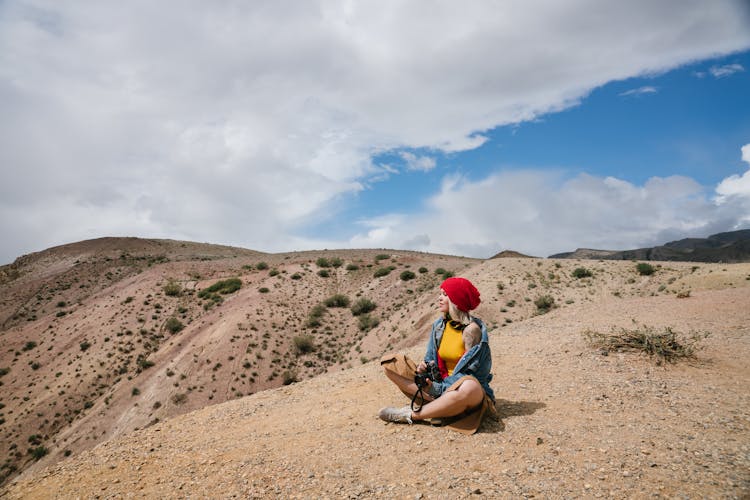 A Woman Sitting On Top Of A Mountain Under Blue Sky