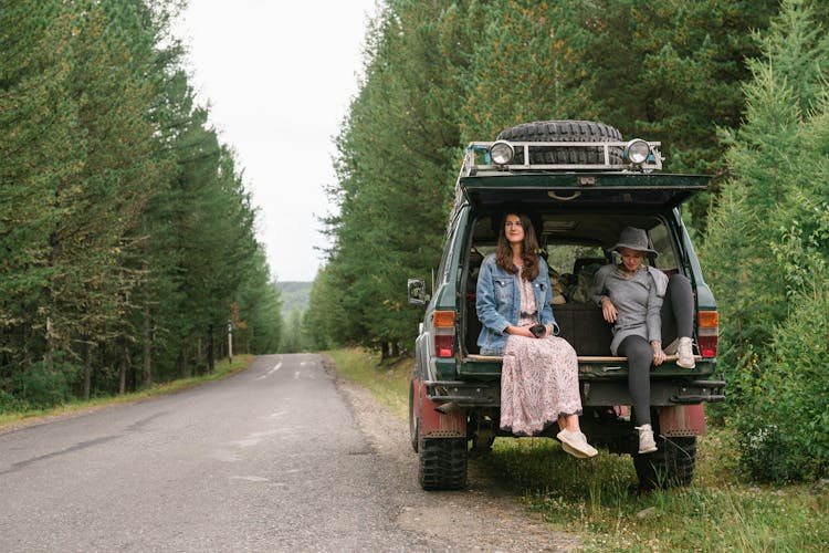 Women Sitting On The Back Of Parked SUV Car