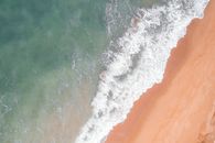 Top view of stormy ocean waves turquoise color crashing against shore with golden sand