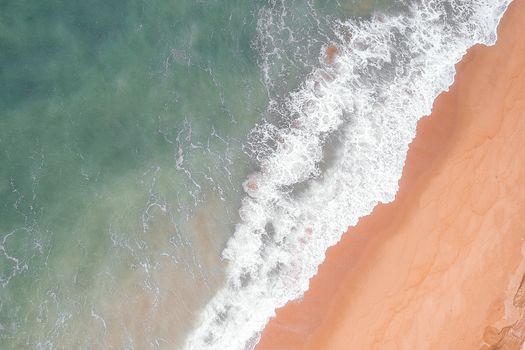 Top view of stormy ocean waves turquoise color crashing against shore with golden sand