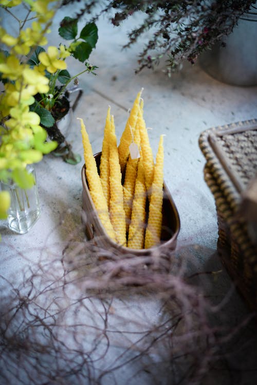 From above of arranged beeswax candles in container placed near glass vase with plant branches and basket
