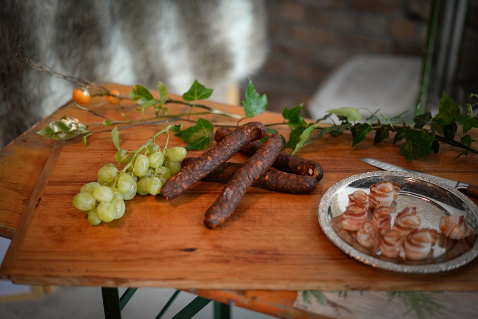 From above of appetizing sausages placed near branch of grapes and bacon plate on wooden board