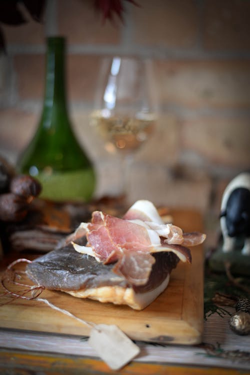 Wooden board with jamon placed against glass of wine and bottle on table