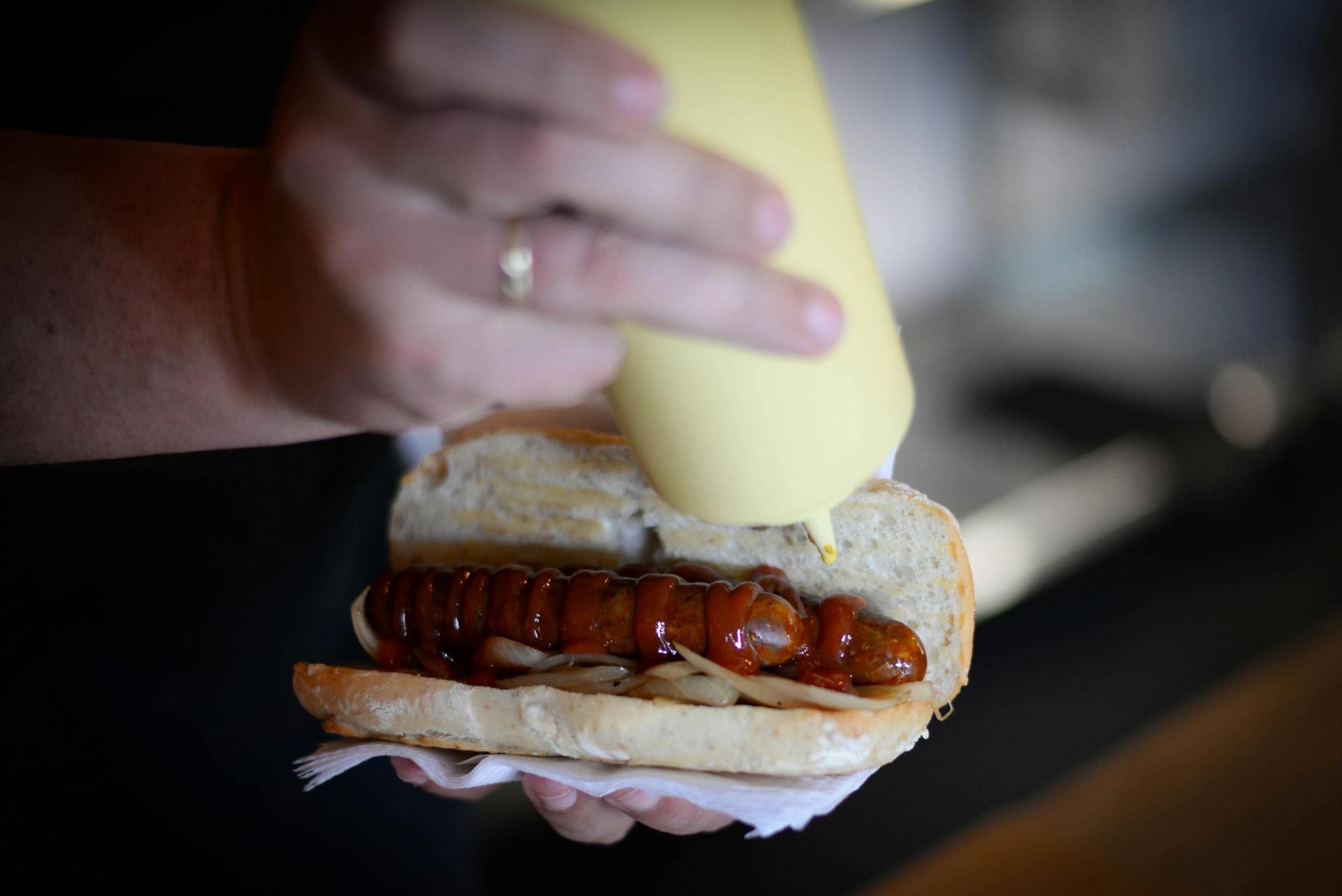 From above of crop anonymous chef putting sauce on roasted sausage in hot dog while selling fast food