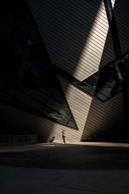 A person stands in sunlight against the dramatic architecture of Toronto's ROM.