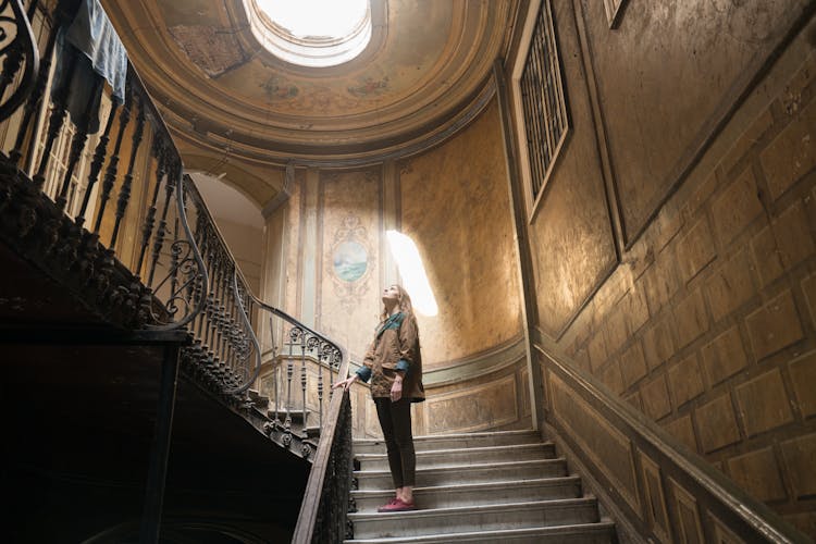 A Woman Standing On The Step Of A Wooden Staircase While Looking Up