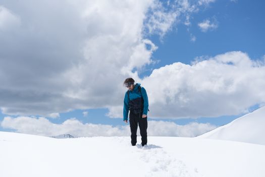 一名孤独的徒步旅行者身穿蓝色夹克，站在雪山上，头顶是多云的天空