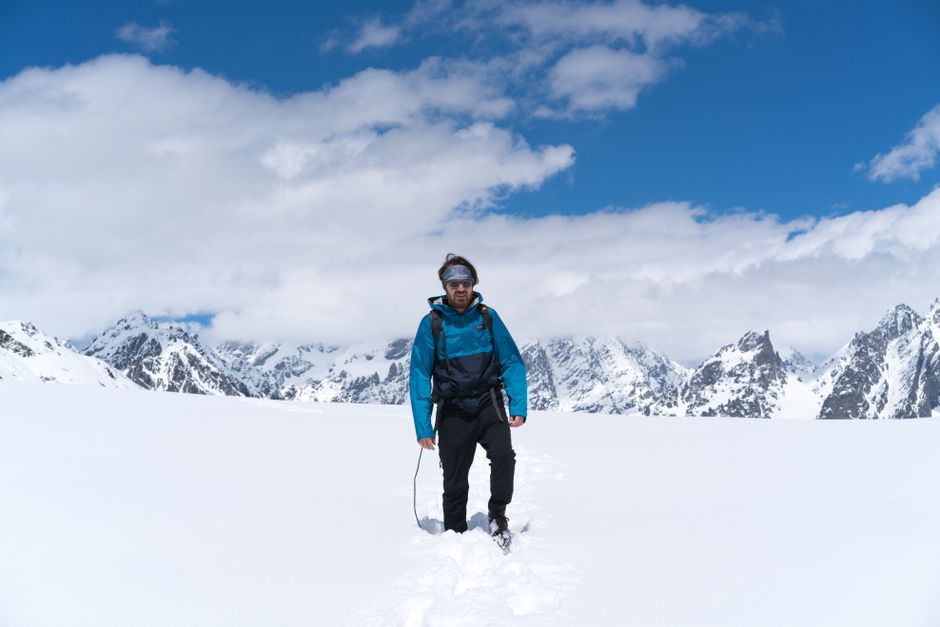 A man hiking through a snowy mountain range under a bright blue sky, embodying adventure.