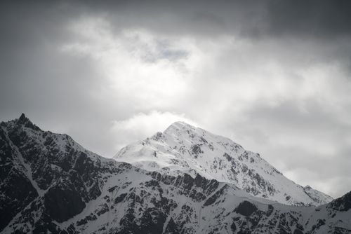 Free Stunning snow-covered mountain peaks beneath a dramatic cloudy sky, capturing the essence of winter's chill. Stock Photo