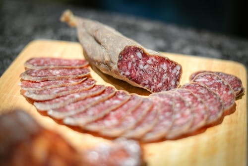 Cold cuts of delicious smoked sausage placed on wooden board amidst sausage slices in kitchen