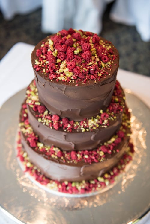From above yummy tiered chocolate cake decorated with ripe raspberries and nuts served on table