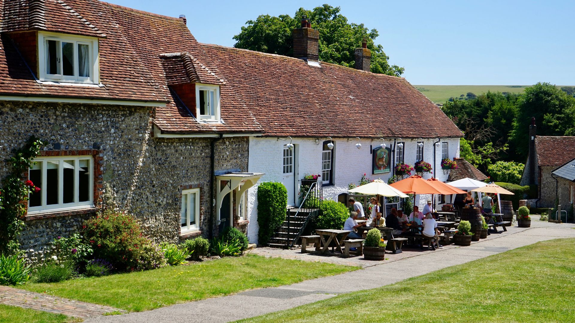 Charming countryside house with people enjoying an outdoor cafe area on a sunny day.