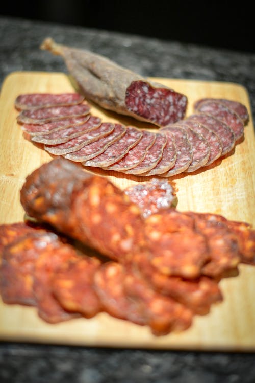 Free Composition of yummy cold cuts with cured sausages slices arranged on wooden board on table in kitchen Stock Photo