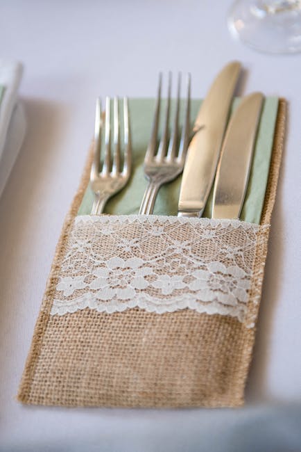 From above cutlery in lace pouch served on dining table with white cloth before banquet