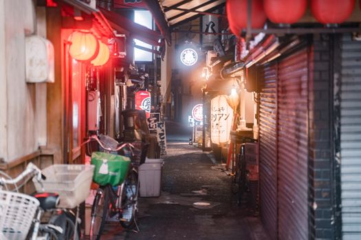 A bustling Japanese alley in Osaka at night, adorned with colorful lights and signs.