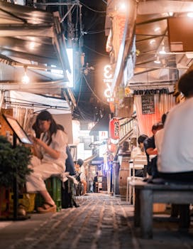 Lively Osaka alleyway at night with people dining at outdoor restaurants, capturing vibrant city life.