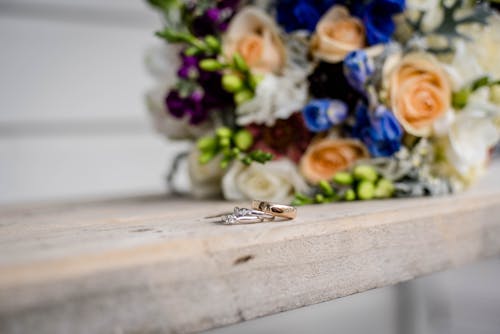 Shiny rings with precious stones near bright blossoming flower bouquet on wooden surface on wedding day