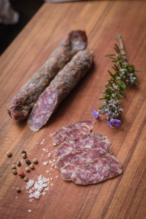 Free From above of tasty salami slices near sea salt and peppercorns with aromatic rosemary Stock Photo