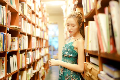 Free Side view pensive slender Asian female in blue summer dress standing between bookshelves in modern library of university Stock Photo
