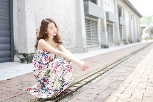 Free Full length calm young Asian female in stylish maxi dress sitting on haunches on paved street in sunlight Stock Photo