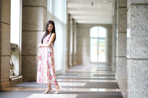 Free Full length charming slim Asian female wearing pink summer dress standing calmly in light sunny hallway and looking down shyly Stock Photo