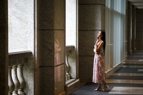 Free Side view full body dreamy young Asian female wearing summer maxi dress standing in light spacious hallway and looking out window pensively Stock Photo