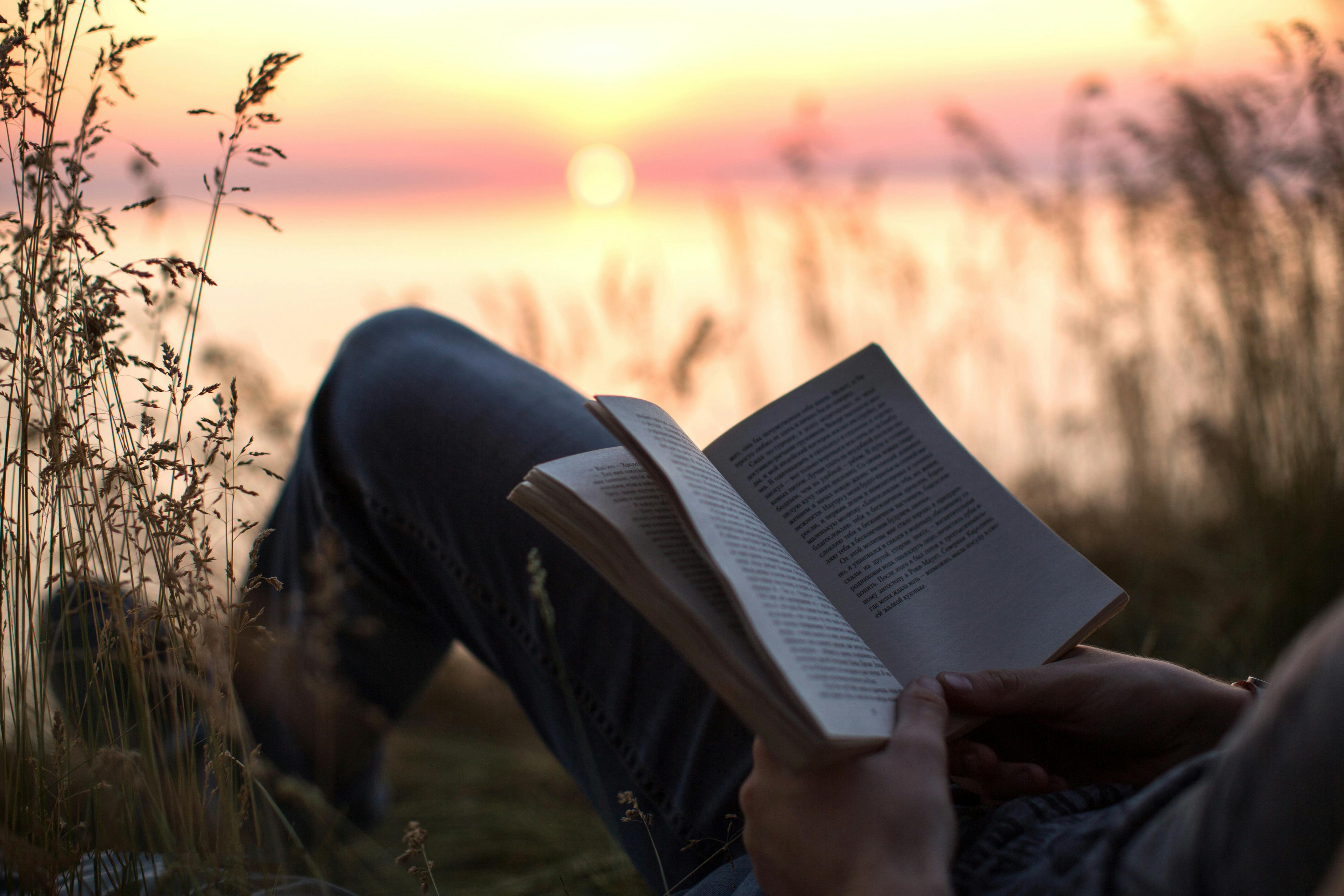 person in black pants reading book during sunset