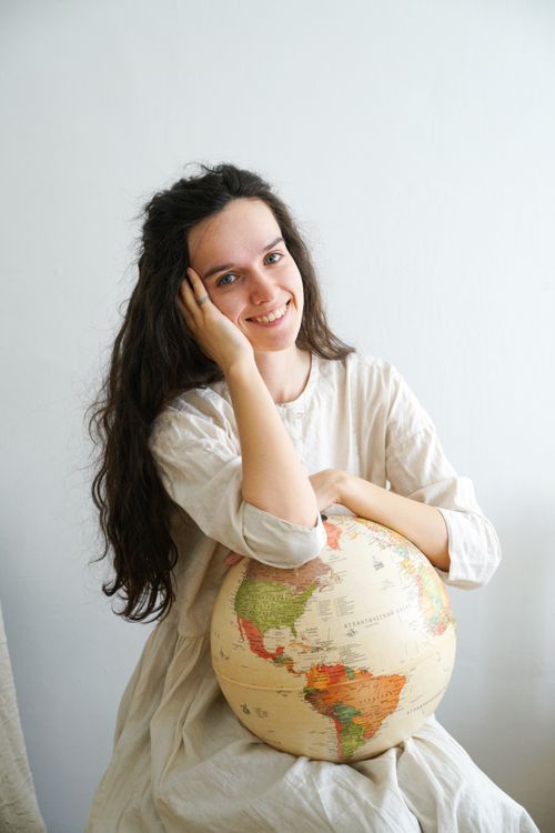 Free Cheerful woman in white dress holding a globe, seated indoors. Stock Photo