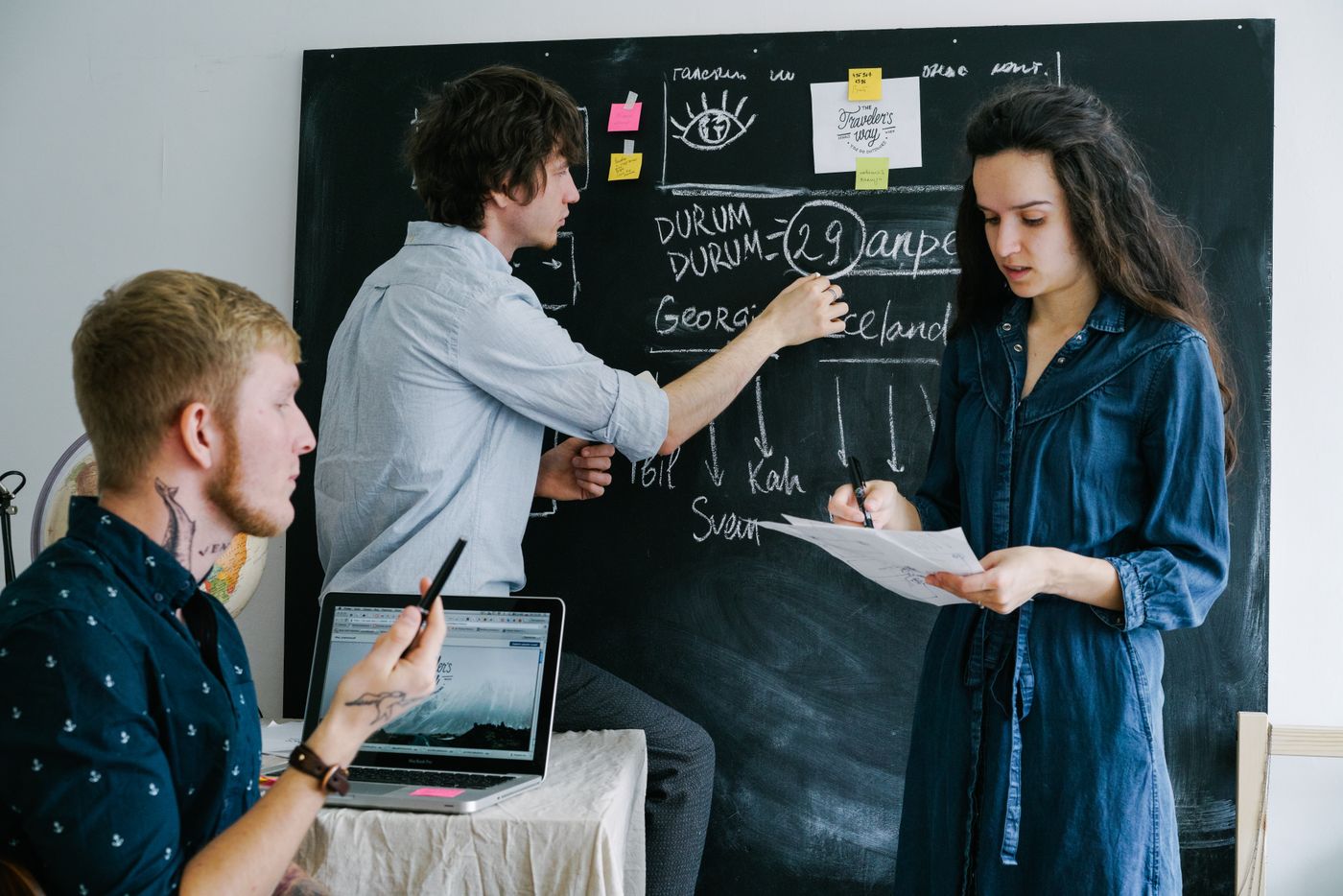 Design students discussing work near a blackboard