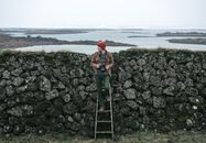 Woman in Red Knit Cap and Blue Denim Jacket Standing on Rock Wall