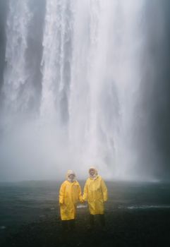 一对穿着黄色雨衣的夫妇，在薄雾笼罩的瀑布前相拥，迎接冒险