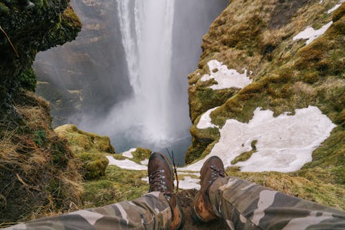 Man Sitting on the Edge of a Mountain with a View on a Waterfall