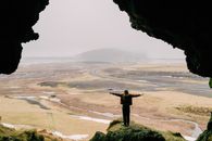 Woman Spreading Arms on Top of Cliff Overlooking Beach
