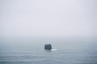雾天，平静的海面上矗立着一块孤石，营造出宁静而孤寂的氛围