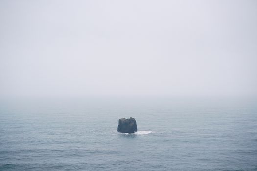 雾天，平静的海面上矗立着一块孤石，营造出宁静而孤寂的氛围