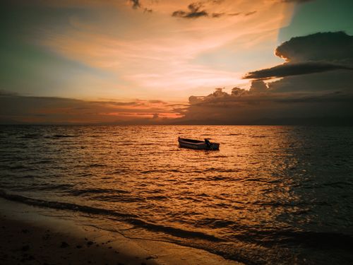 Free A serene sunset scene featuring a solitary boat on a calm sea, casting a warm glow. Stock Photo