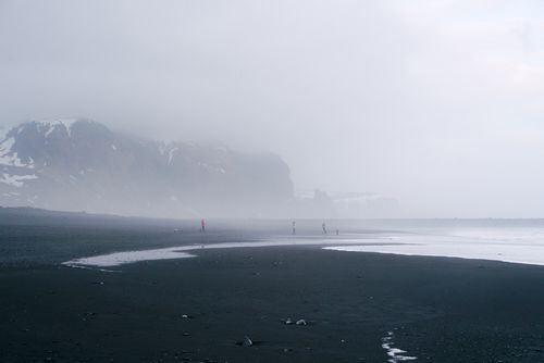 Free Misty coastal landscape with people walking along a foggy beach. Stock Photo
