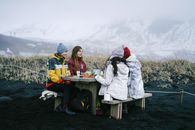 Friends gather for a winter picnic amid Iceland's scenic mountains. Embrace the chill with cozy jackets.