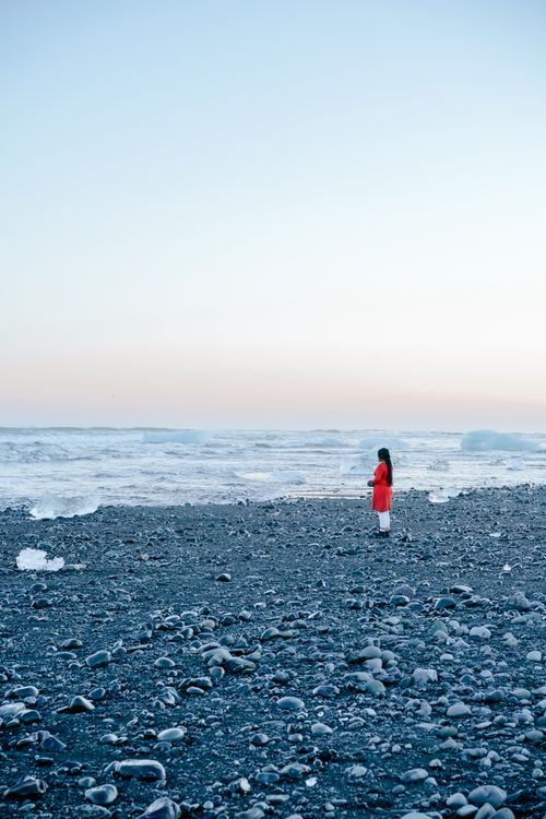 Free A solitary woman stands on a rocky Icelandic beach amid ice under a clear sky. Stock Photo